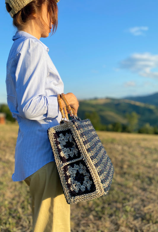 Borsa uncinetto a bauletto Aurora blu indossata da una donna in un paesaggio naturale con collina sullo sfondo.