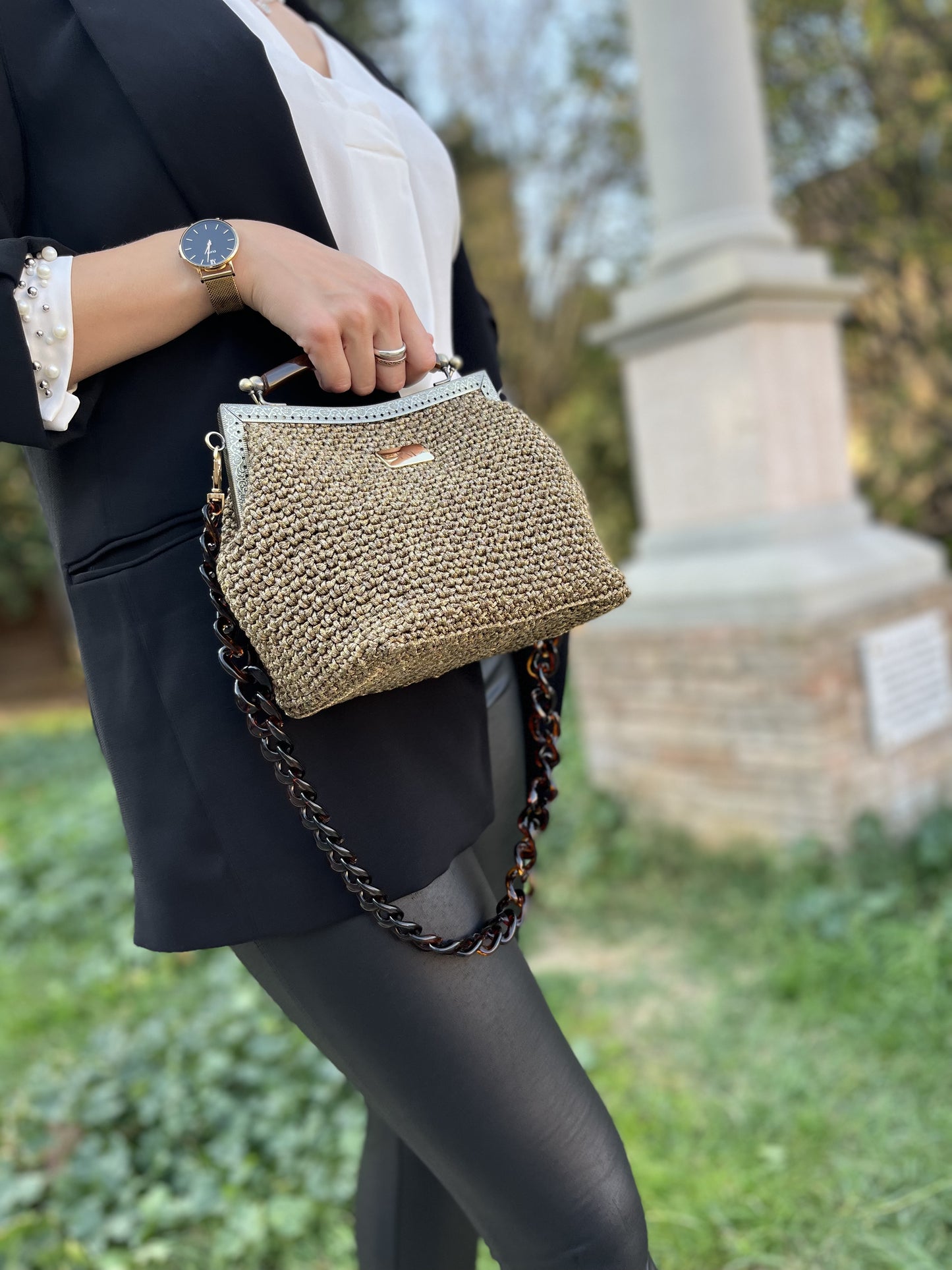 Borsa clutch uncinetto Susanna bronzo indossata da una donna nel parco con catena colorata.
